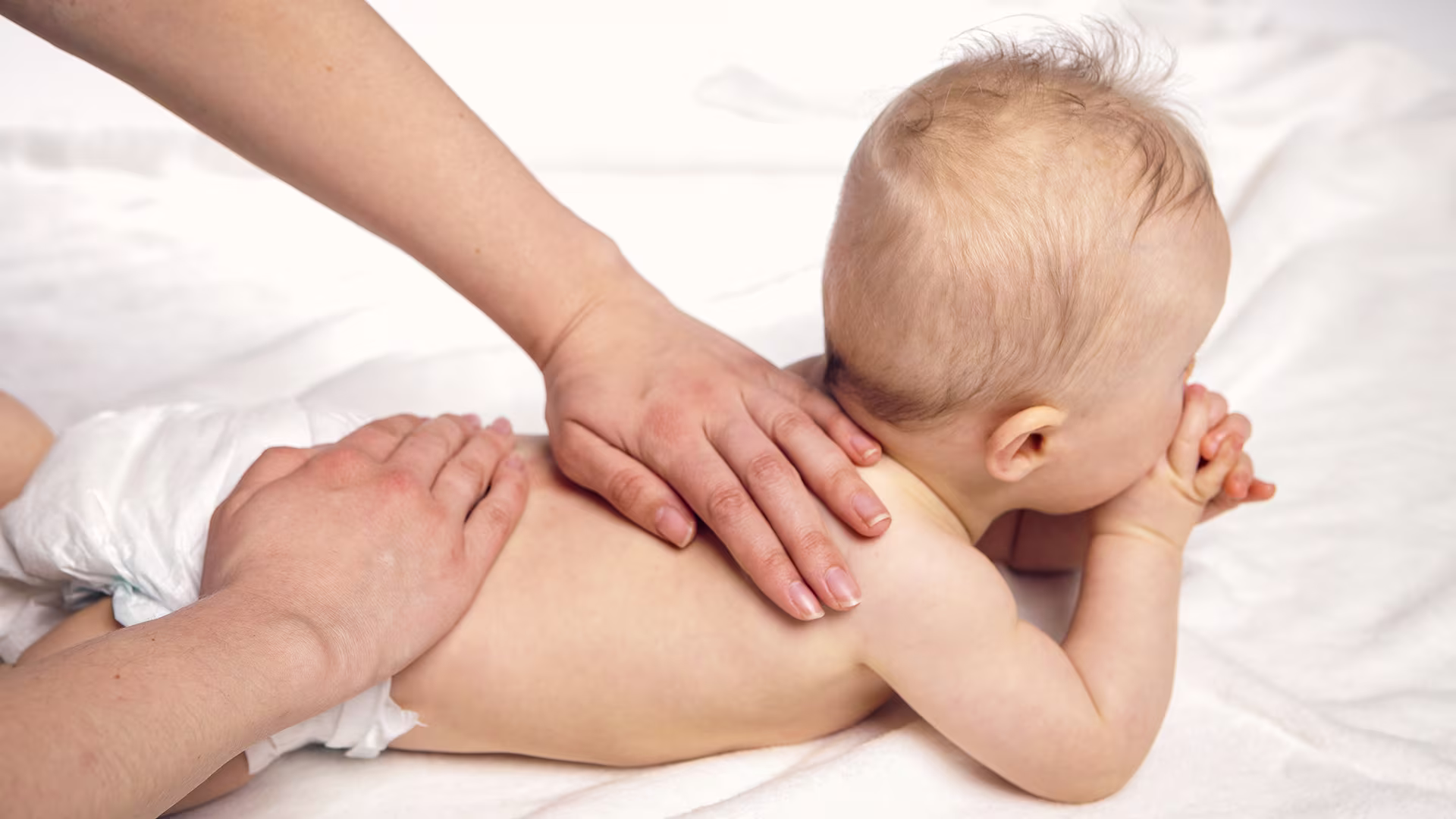 Baby lying on its tummy receiving physical therapy 