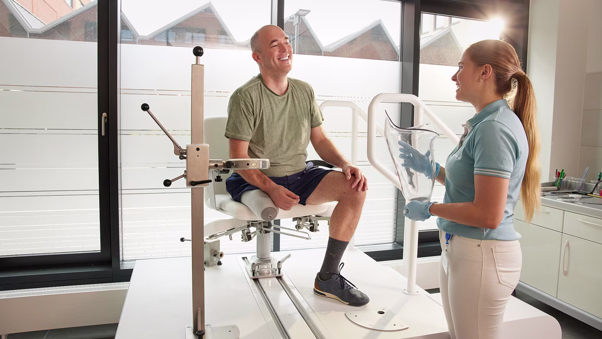 CPO holding a custom test socket and smiling at a transtibial amputee patient in a patient care center.