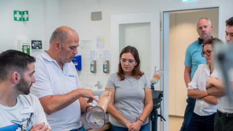Ein Ottobock Mitarbeiter hält eine Fußprothese in der Hand und zeigt diese den umstehenden Seminarteilnehmern.