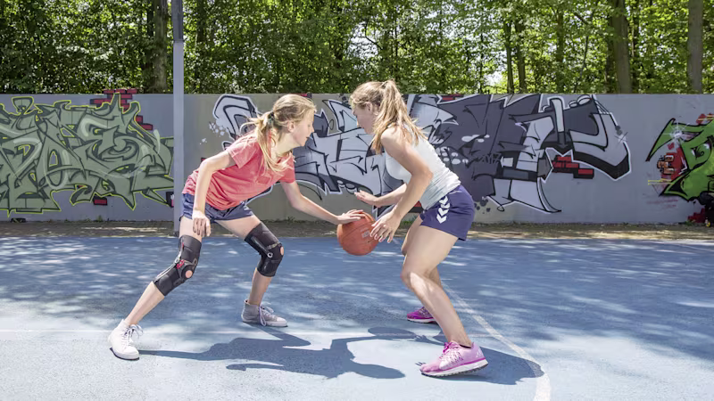 Two young girls playing basketball wearing sports gear and a brace on both knees for support