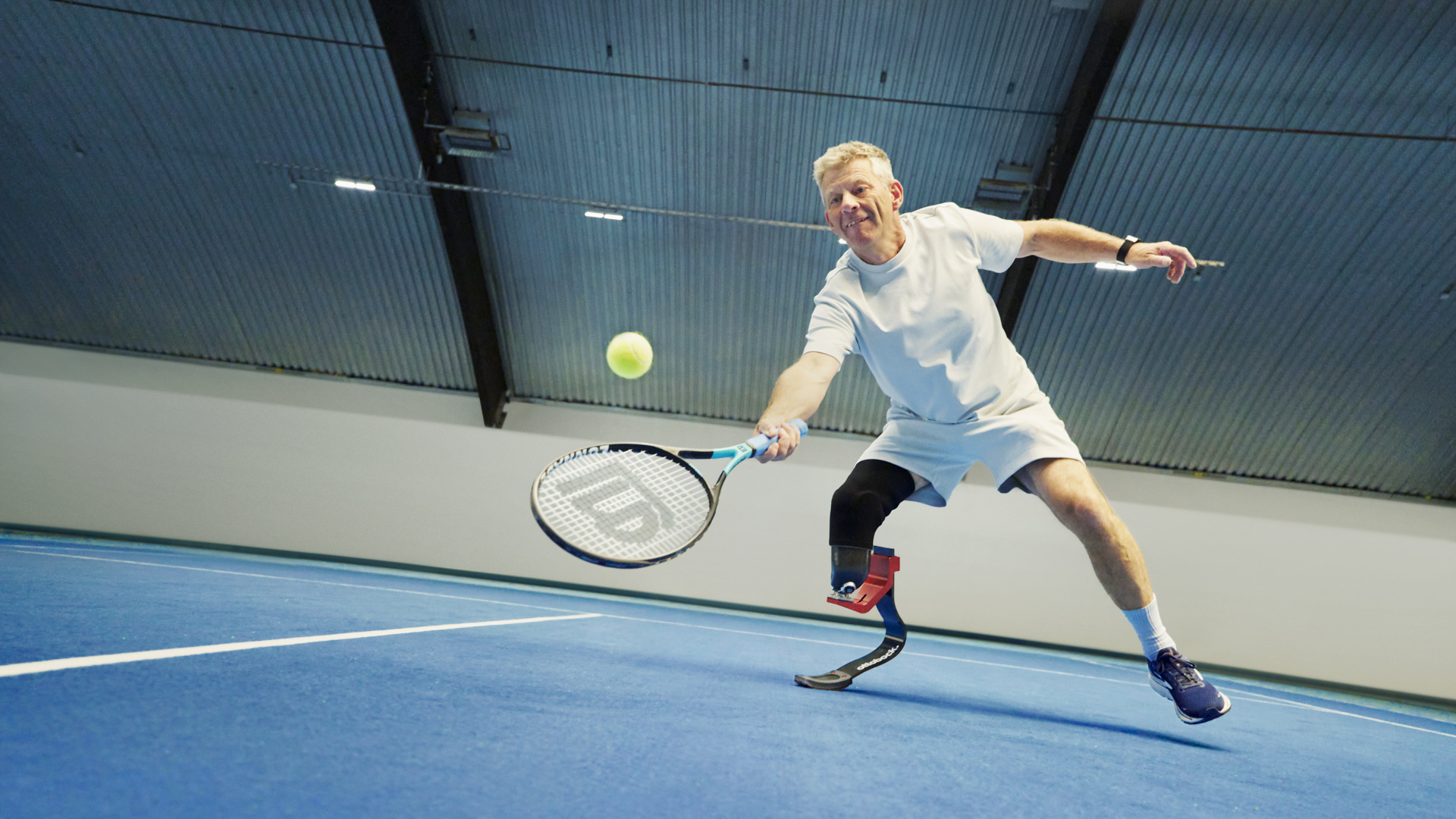 Ein beinamputierter Mann spielt in einer Sporthalle Tennis. Er trägt dabei eine Sportprothese von Ottobock.