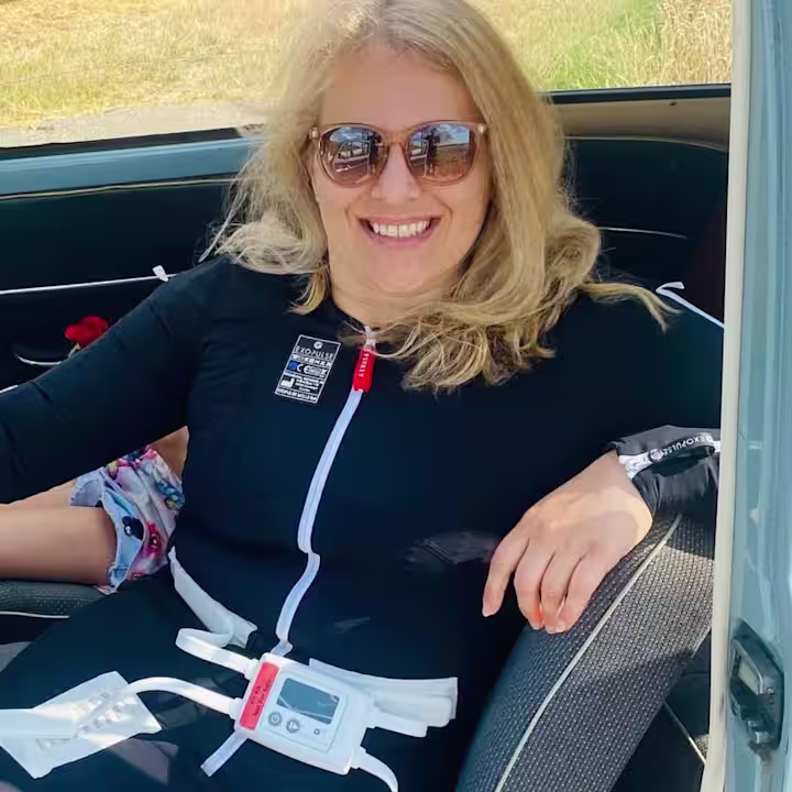 Kerstin sitzt in einem Auto und trägt dabei den Exopulse Mollii Suit.