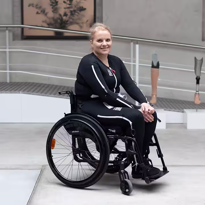 Eine weibliche gelesene Person trägt den Exopulse Mollii Suit und sitzt im Avantgarde Rollstuhl von Ottobock.