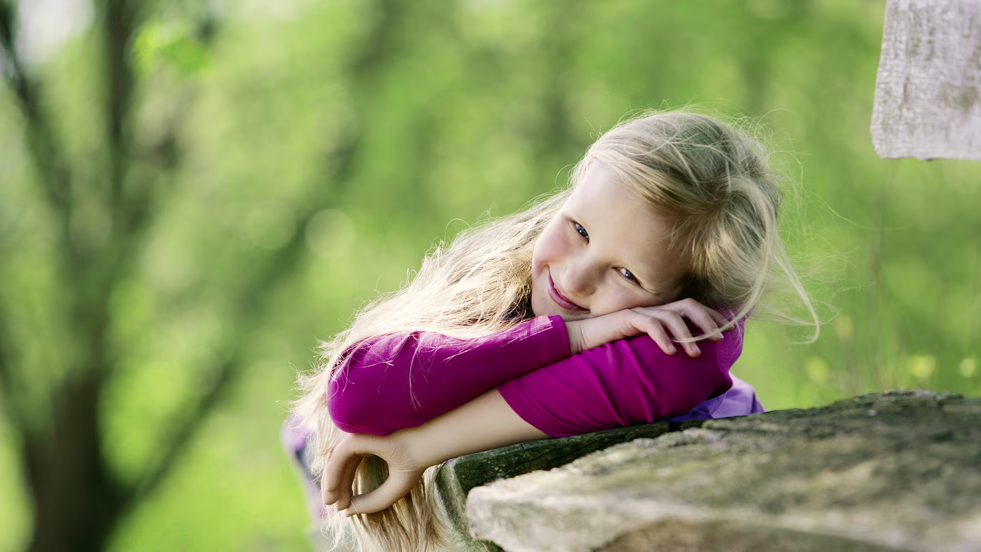 Ein junges Mädchen stützt sich im Wald an einem Ast ab, dabei trägt sie die Kinderhand