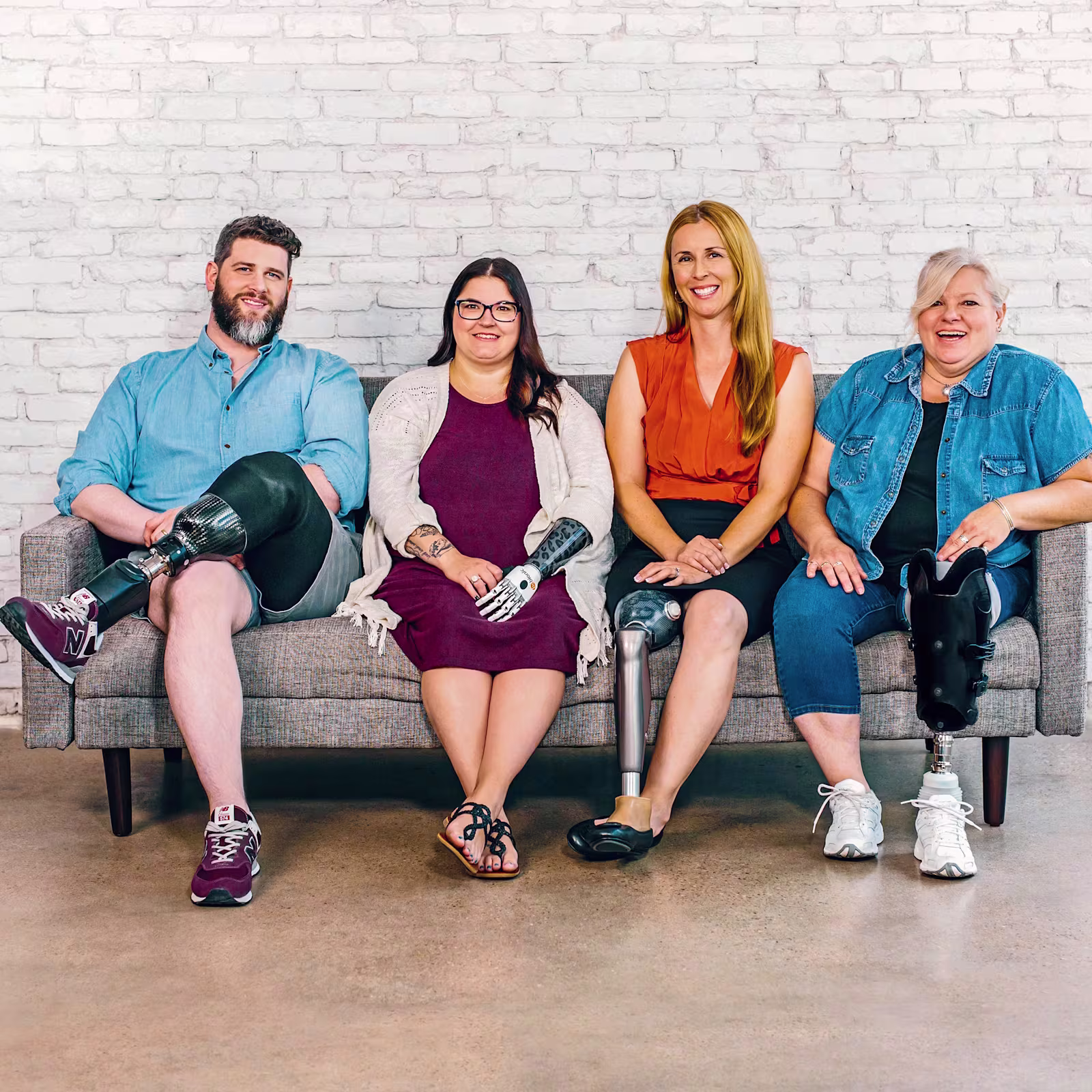 Four people sitting on a bench. A man with a below the knee prosthetic leg, a woman with a bebionic hand, a woman with a C-Leg prosthetic knee joint and a woman with a trans-tibial prosthesis.