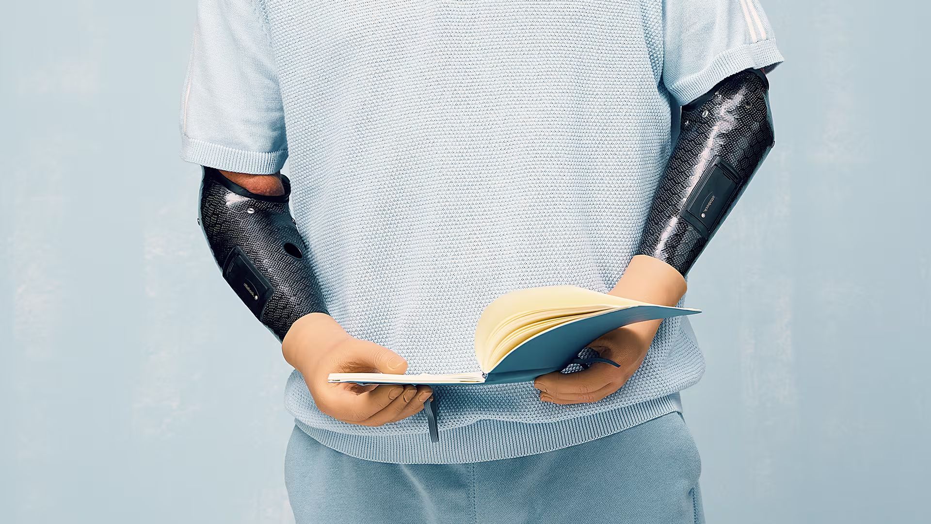 A bilateral arm amputee uses his bionic arms and Ottobock MyoSkin Natural gloves to hold and read a book
