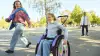 Nomine zit in the Kidevo rolstoel, rijdend door het park met haar moeder.