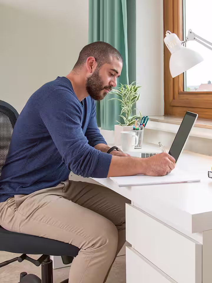 Ein Mann sitzt am Schreibtisch und arbeitet am Laptop.