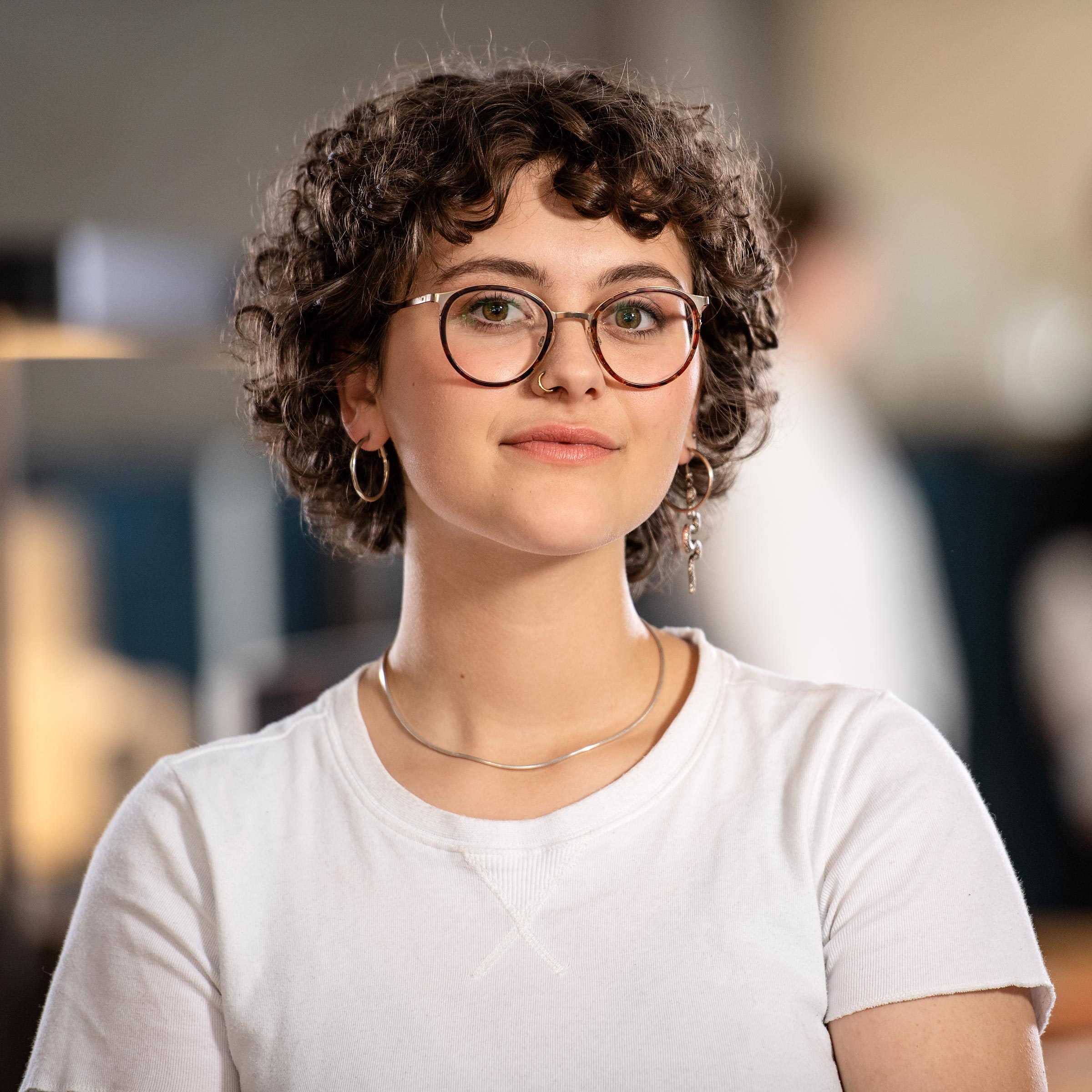 Ritratto di Lina in camicia bianca e collana, viso sfocato per la privacy.