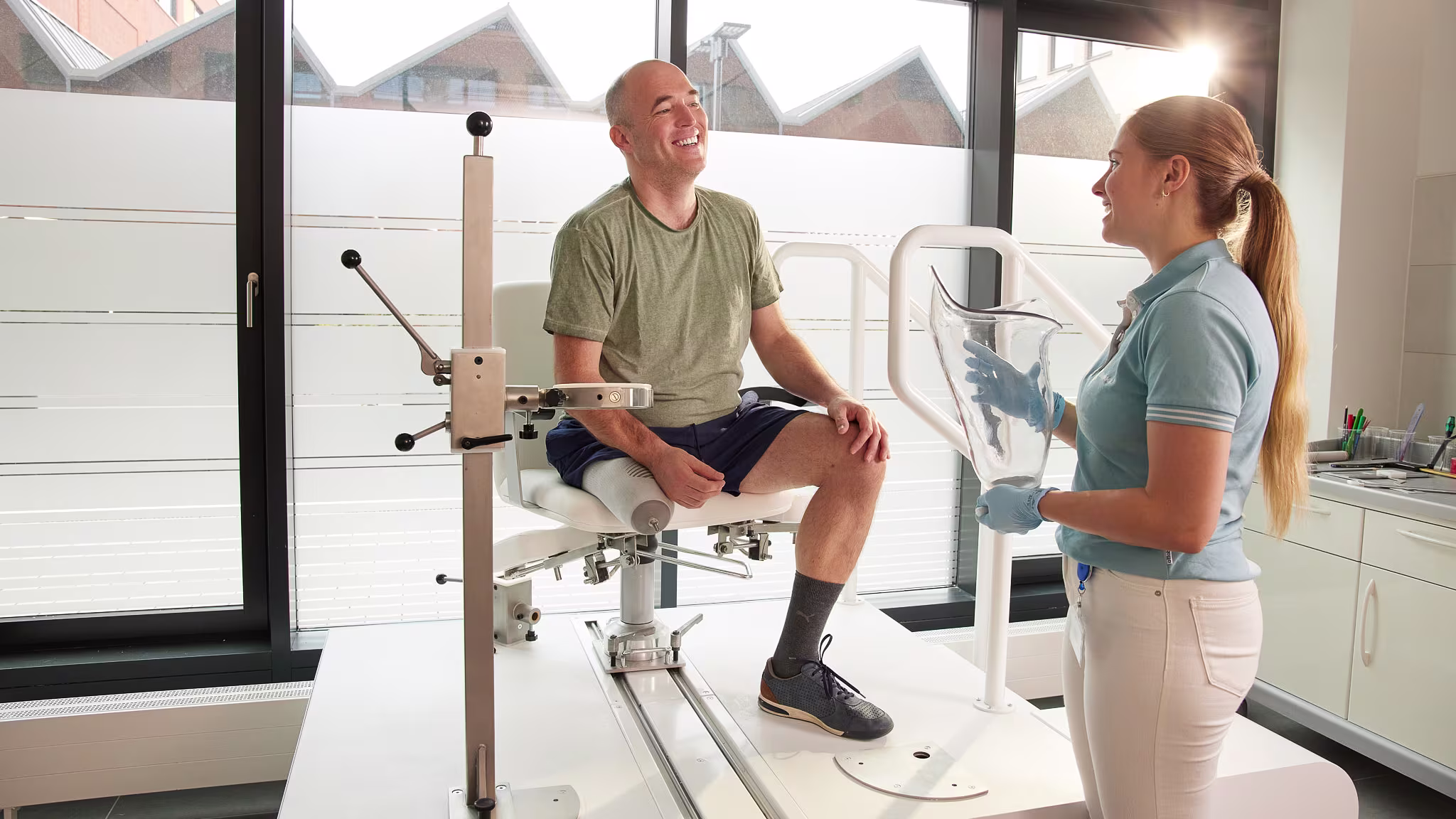 Ein amputierter Mann sitzt vor einer Orthopädietechnikerin, die einen MyFit TF Interimsschaft von Ottobock in der hand hält und die beiden lächeln sich an.