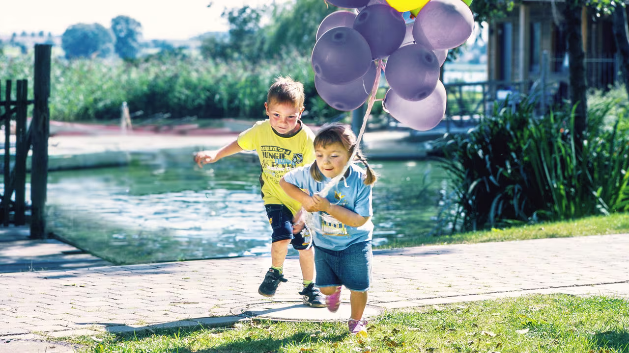 Eine junge Prothesenträgerin spielt mit einem anderen Kind und hält dabei Luftballons. Sie trägt die Elektrohand 2000 von Ottobock.