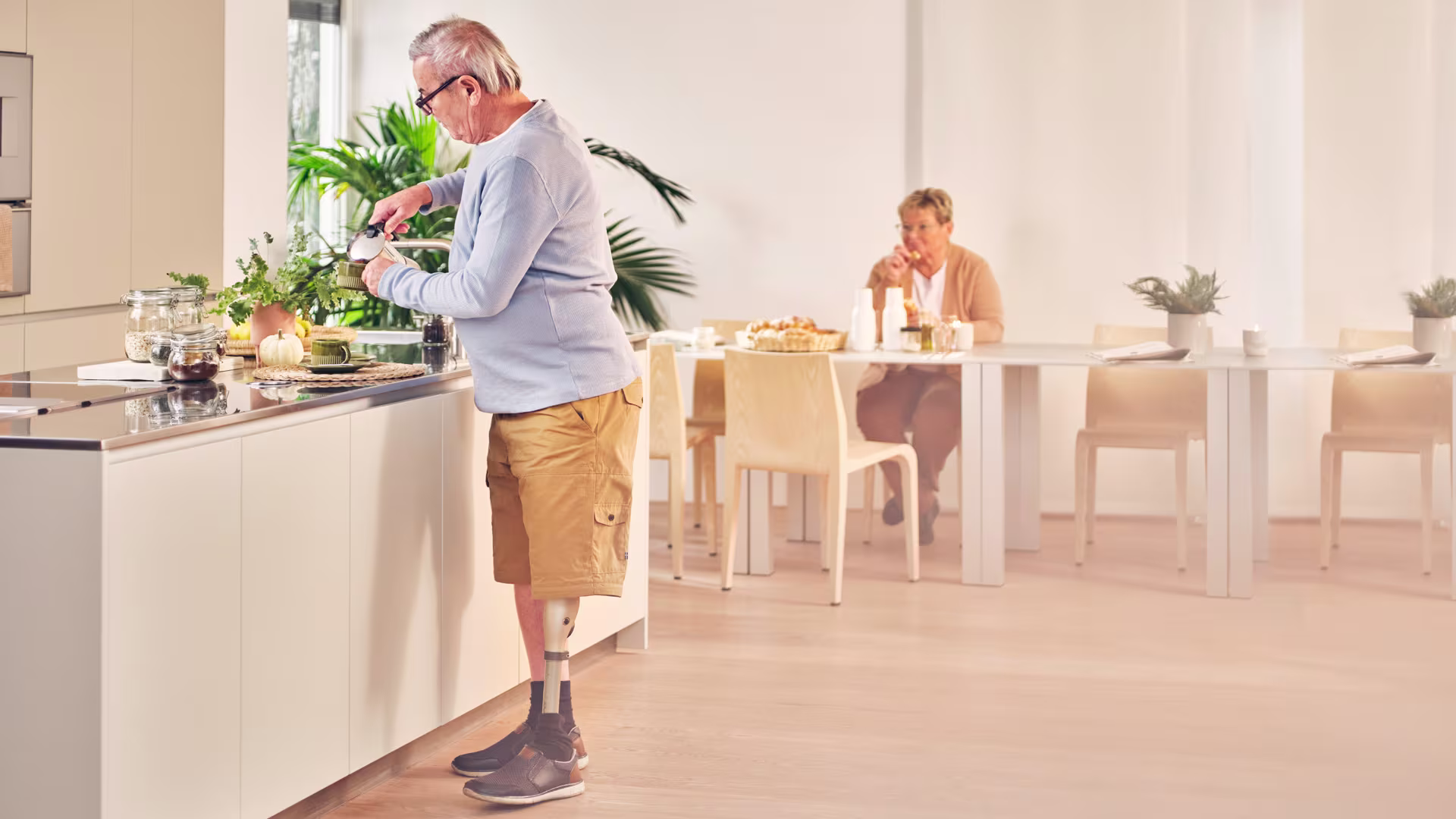 Ein älterer Mann steht in der Küche und bereitet einen Kaffee zu. Er trägt dabei das mechatronische Prothesenkniegelenk Kenevo von Ottobock.