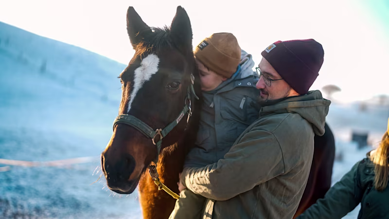 Cerebral palsy patient petting a horse together with his father