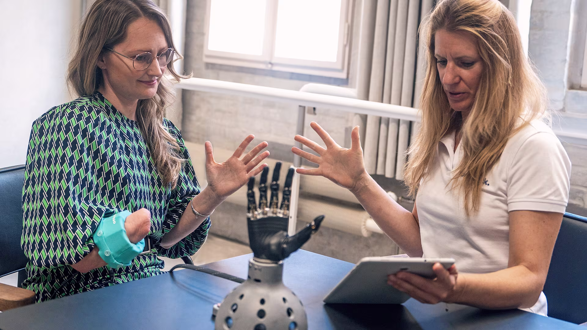 O&P specialist and prosthetic hand user reviewing a prosthetic hand model on a stand while holding a tablet.