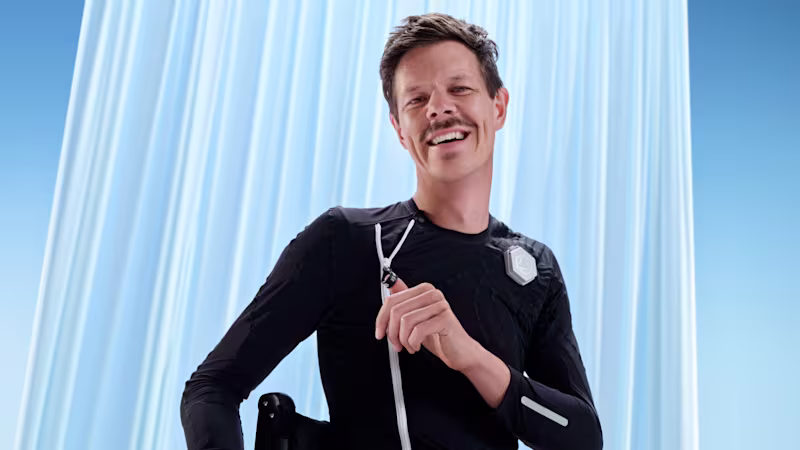 Male person smiles while pulling up the zipper of the Ottobock Exopulse Suit at his upper chest
