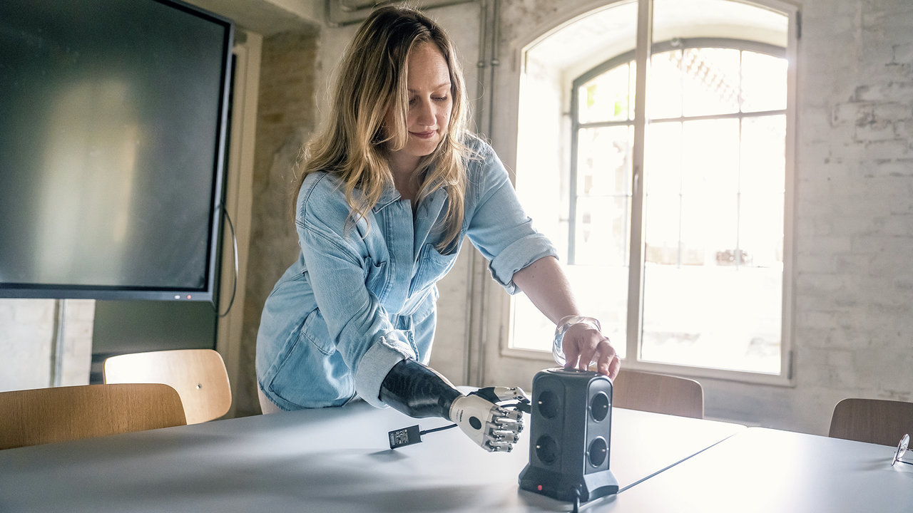Eine Armprothesenträgerin benutzt eine Steckdose im Büro. Sie trägt die bebionic Hand von Ottobock. 