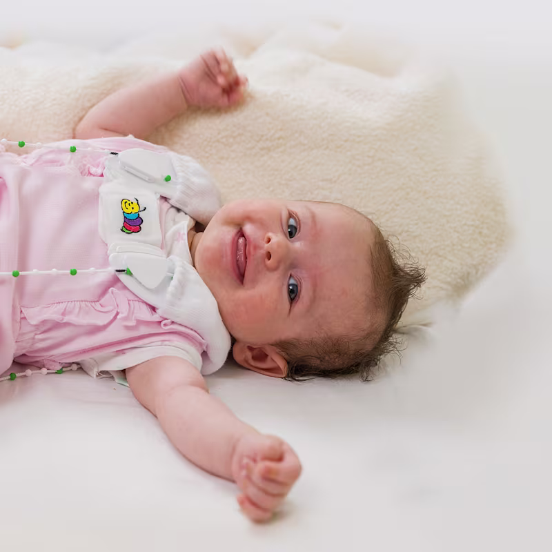 An infant in pink pajamas lays on a fuzzy blanket wearing the Ottobock Tubingen hip flexion and abduction orthosis