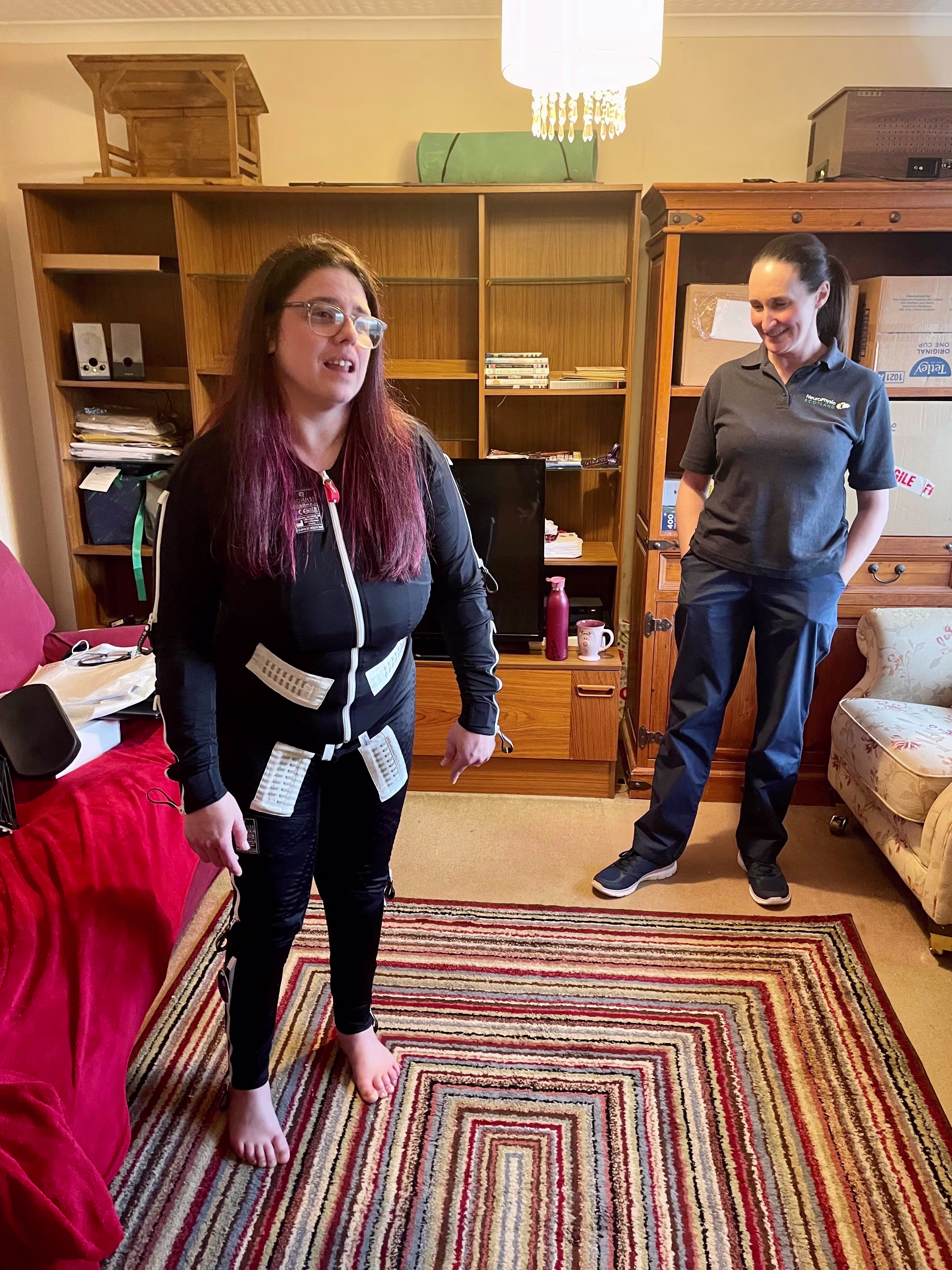 A woman wearing the Exopulse Mollii Suit standing in her house. 