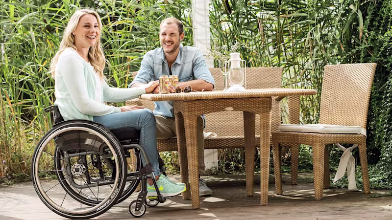 Female person in Ottobock wheelchair sitting at an outdoor table with a man and smiling.