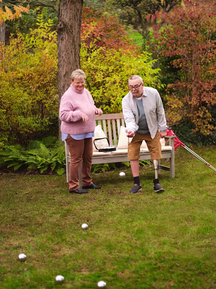 Мужчина пожилого возраста на протезе бедра играет в бочче в саду.