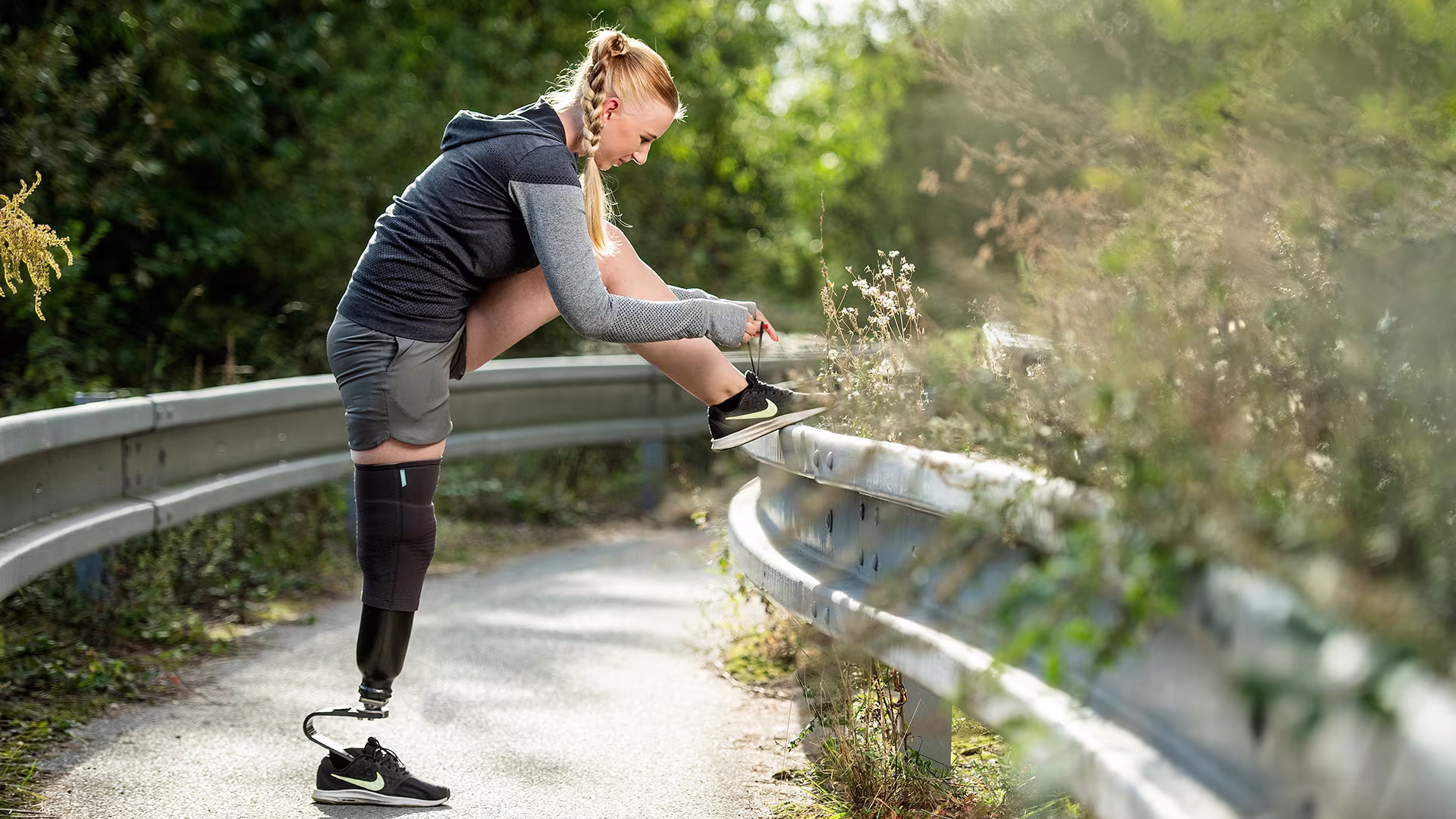 A woman with a Challenger sports prosthesis from Ottobock has her sound side foot resting on a metal barrier while she ties her shoe laces. 