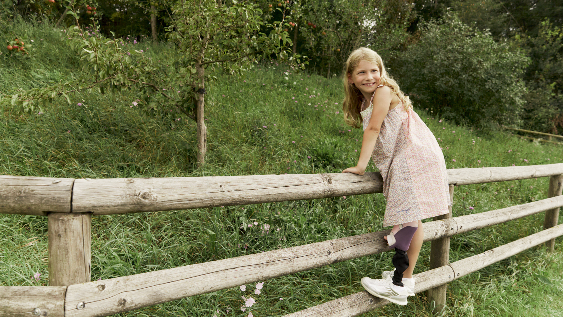 Auf dem Bild sieht man Nora, die auf einen Holzzaun klettert und die Prothesen Maverick junior & movido trägt.