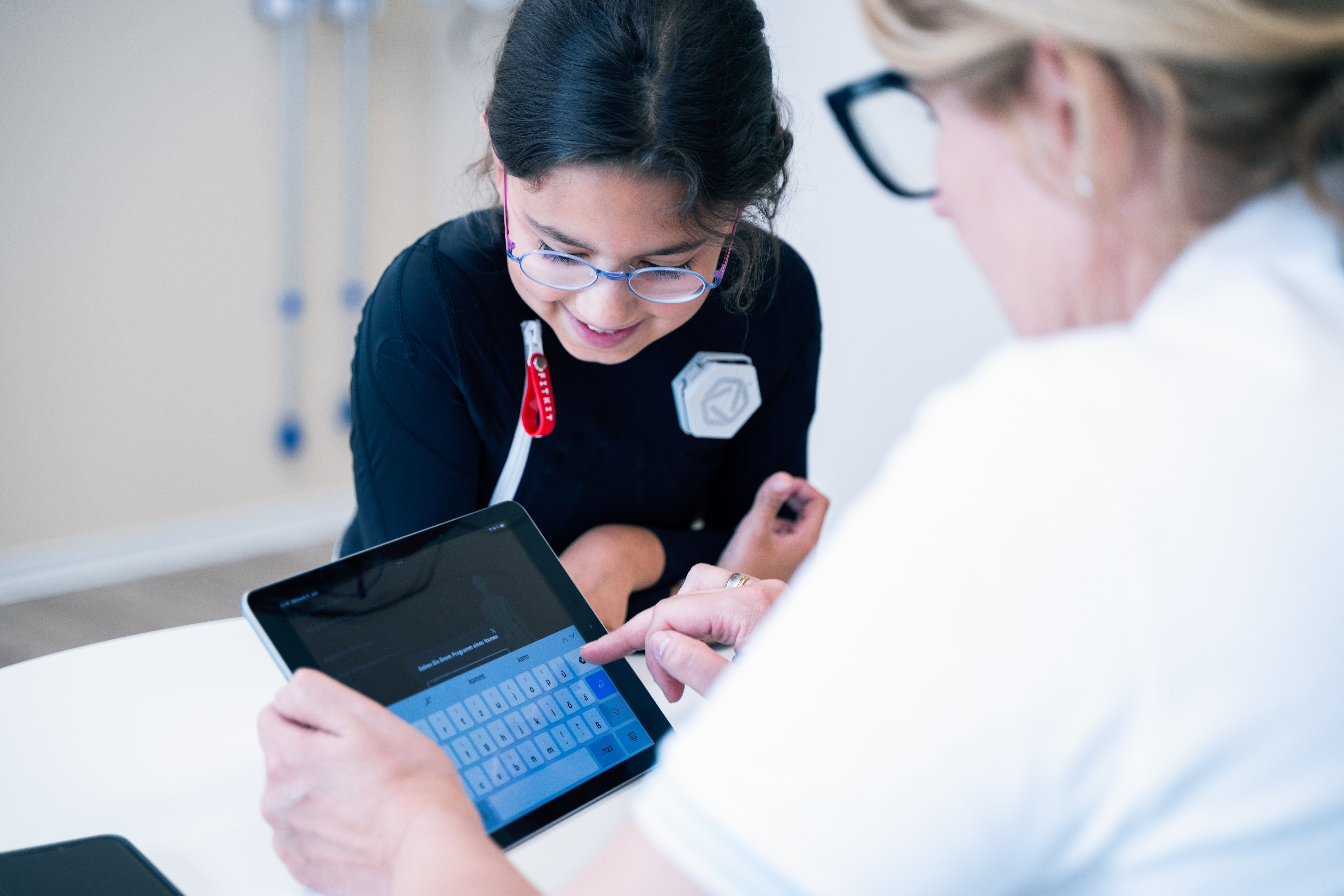 Young girl wearing Exopulse suit working with therapist on a tablet during pediatric rehabilitation session