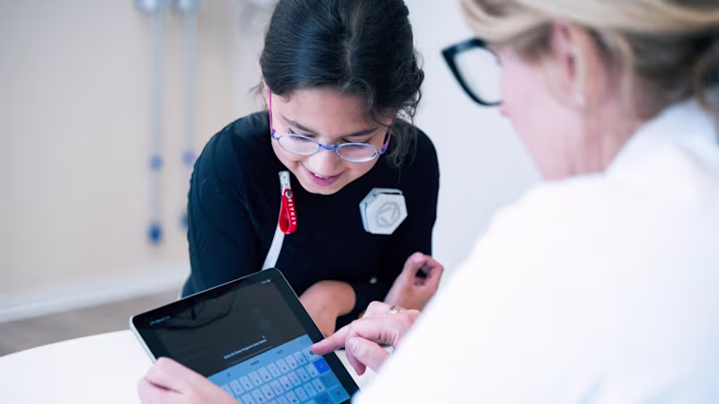 Young girl wearing Exopulse suit working with therapist on a tablet during pediatric rehabilitation session