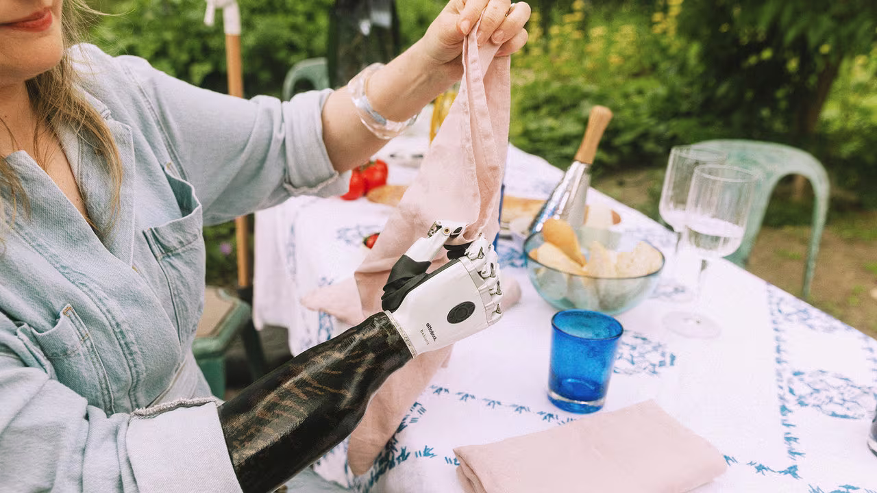 Eine Armprothesenträgerin sitzt an einem Tisch und faltet Handtücher. Sie trägt die bebionic Hand von Ottobock.