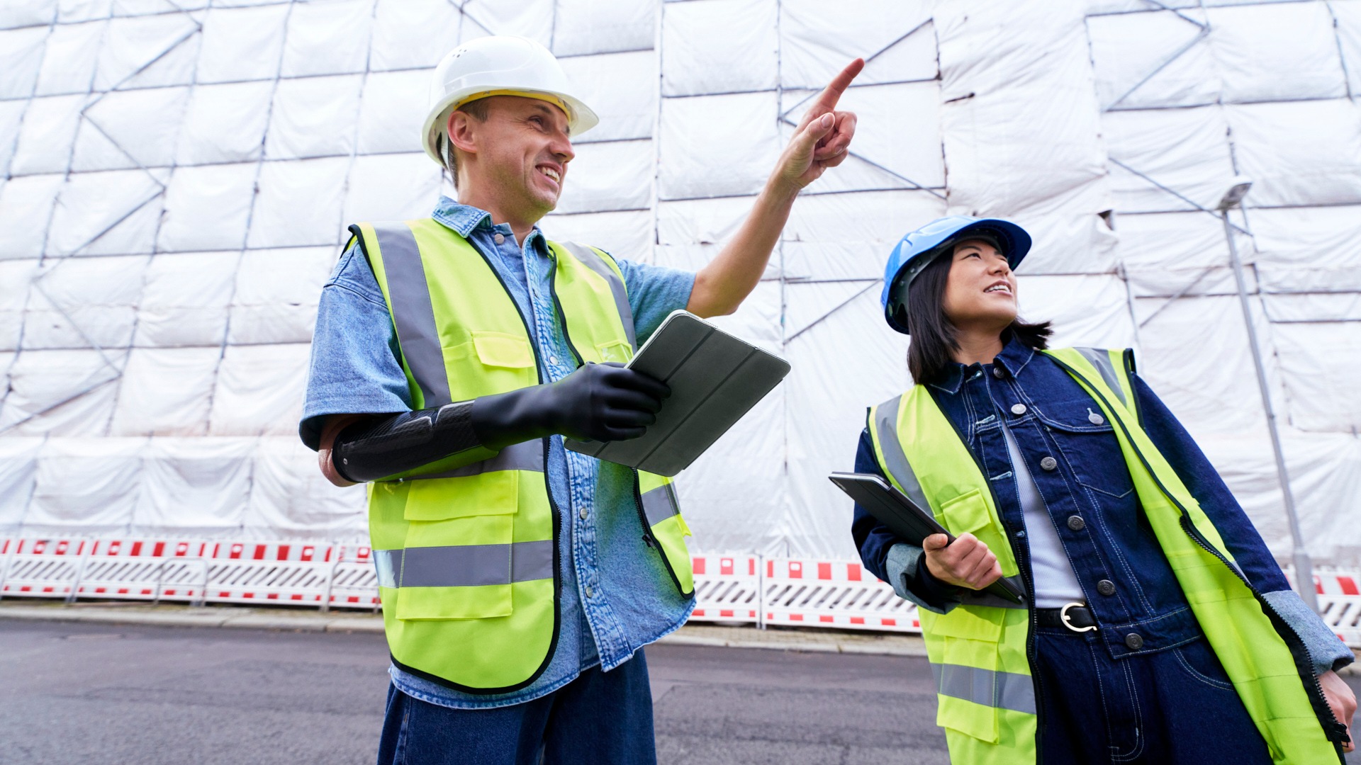 A prosthesis user holds a tablet with their prosthetic hand while standing with a colleague at a construction site.