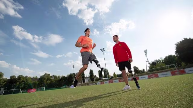 Two men using ottobock. prosthetic legs on a sports field