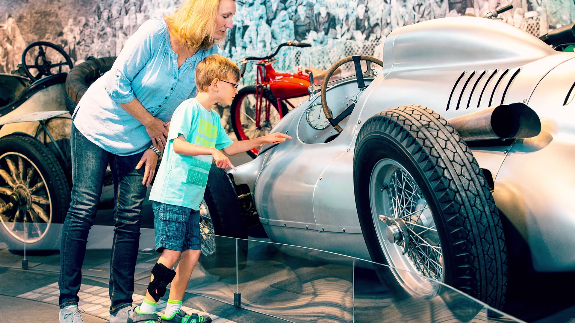 Bambino che indossa Ottobock WalkOn ortotica che esplora auto da corsa d’epoca con l’adulto al museo.