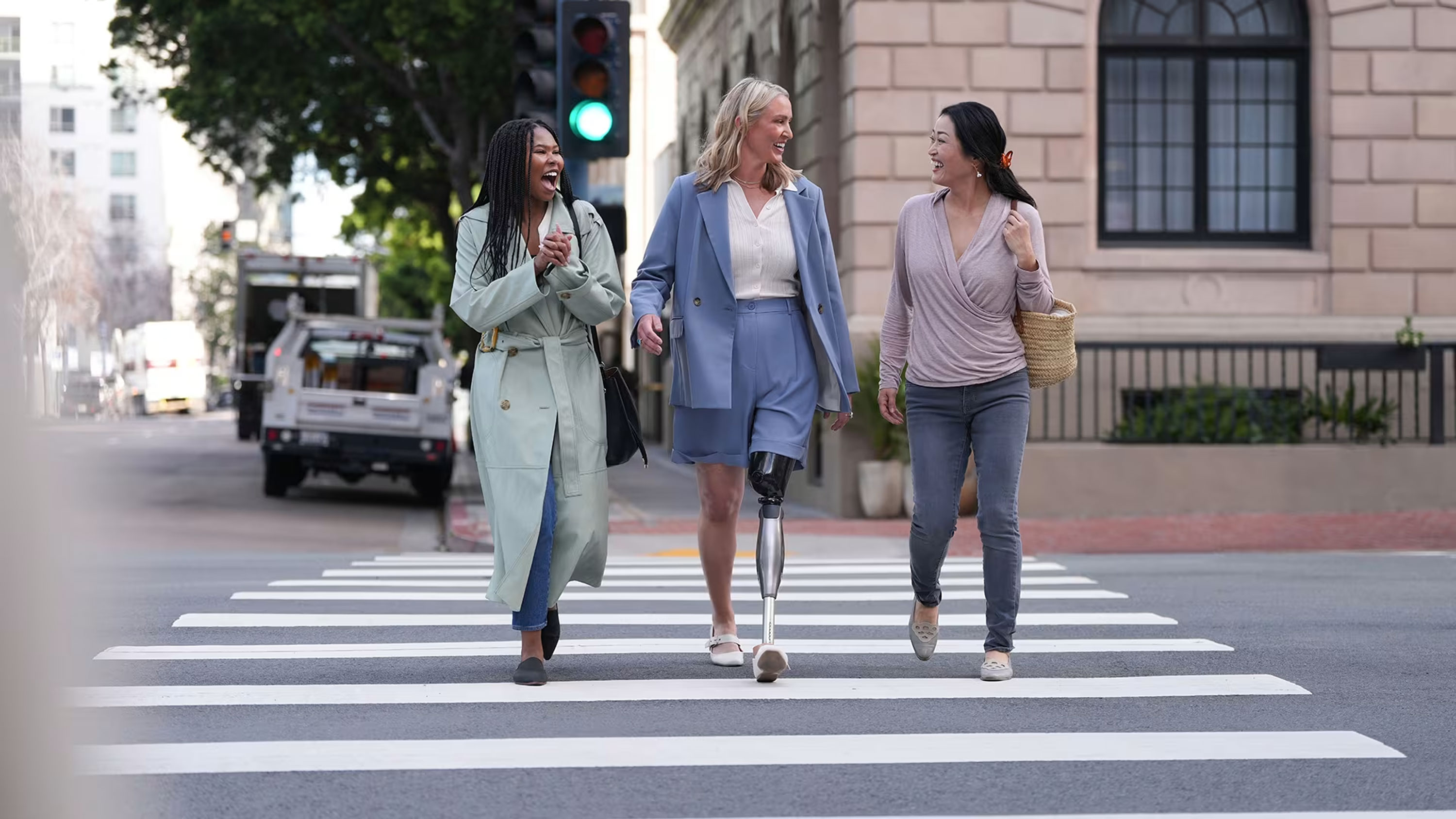A below-knee prosthetic leg user walking across a street with friends in a city