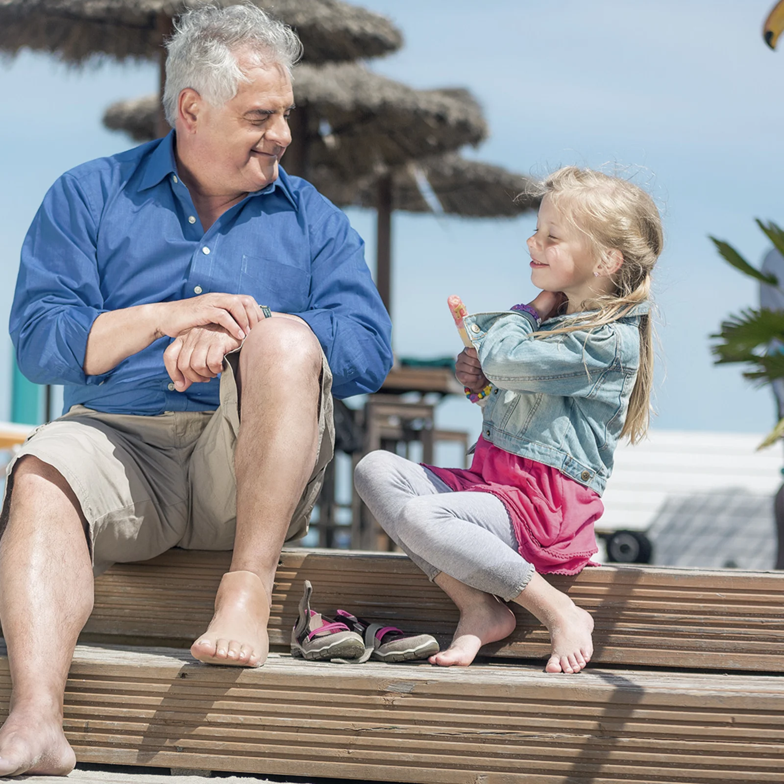 Ein Großvater mit einer Fußprothese genießt mit seiner Enkelin die Sonne am Strand
