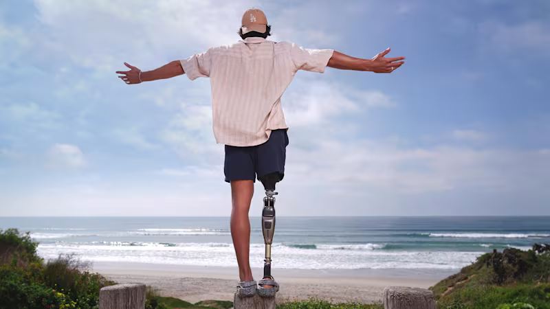 Eine rechtsseitig amputierter Mann steht am Strand mit Blick auf das mehr und breitet die Arme aus, er trägt dabei das mechatronische Prothesenkniegelenk Genium X4 von Ottobock.