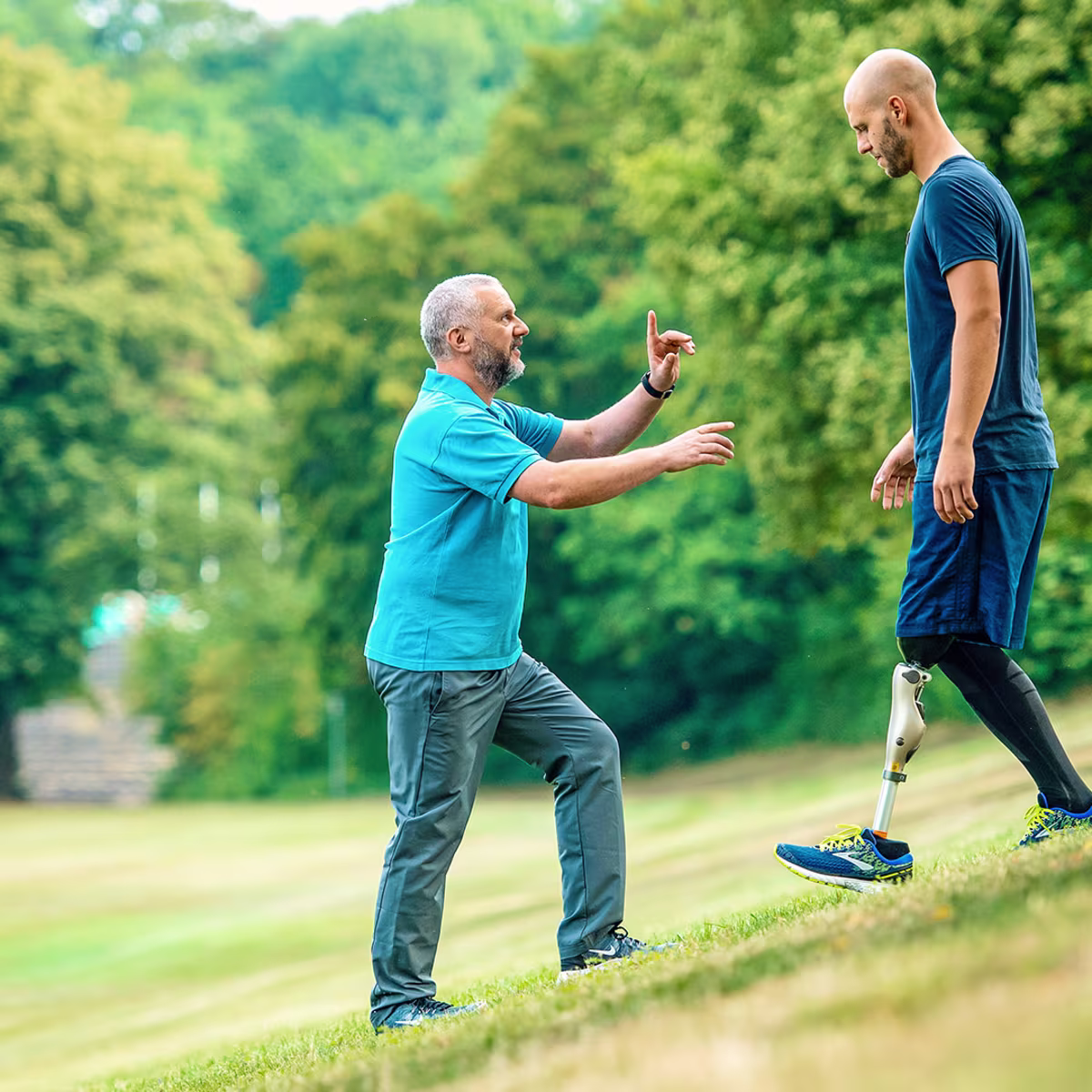 Amputee with Ottobock Kenevo microprocessor knee walking down a steep meadow while getting advice from prosthetist standing in front of him