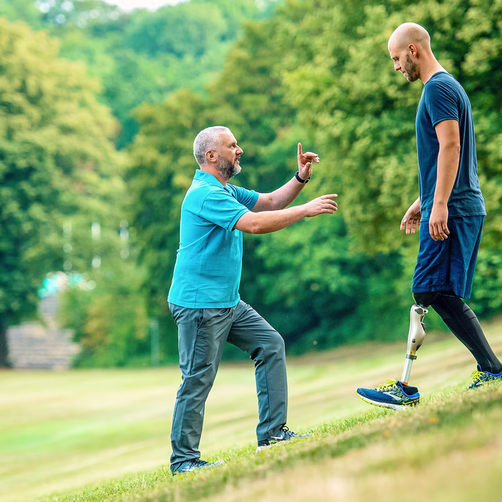 Amputee with Ottobock Kenevo microprocessor knee walking down a steep meadow while getting advice from prosthetist standing in front of him