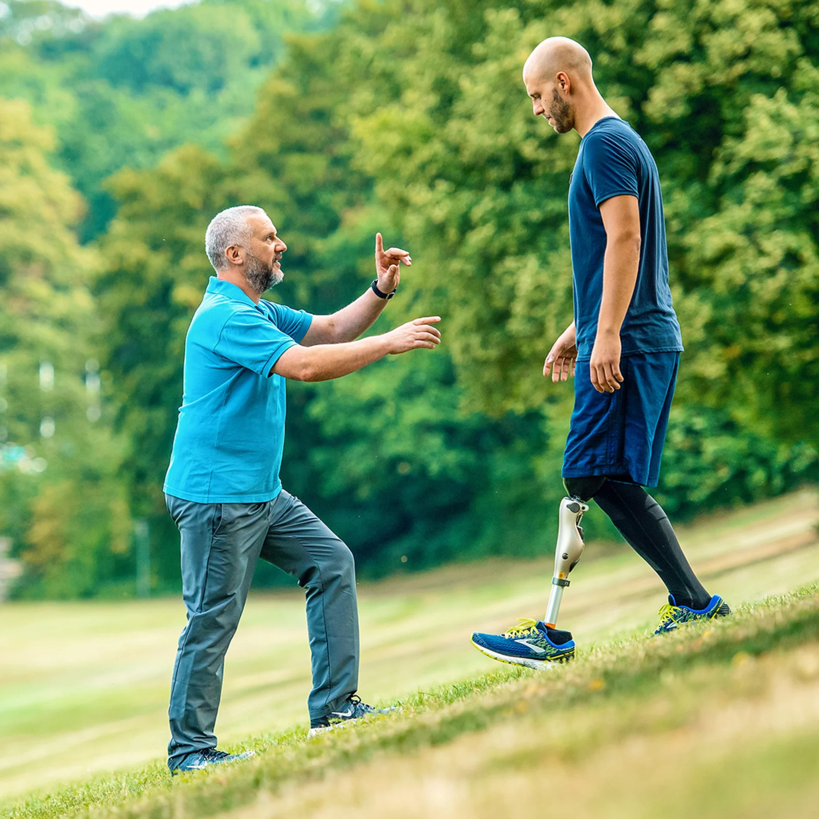 Amputee with Ottobock Kenevo microprocessor knee walking down a steep meadow while getting advice from prosthetist standing in front of him