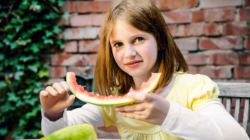 Child with Ottobock hand prosthesis eating a slice of watermelon.
