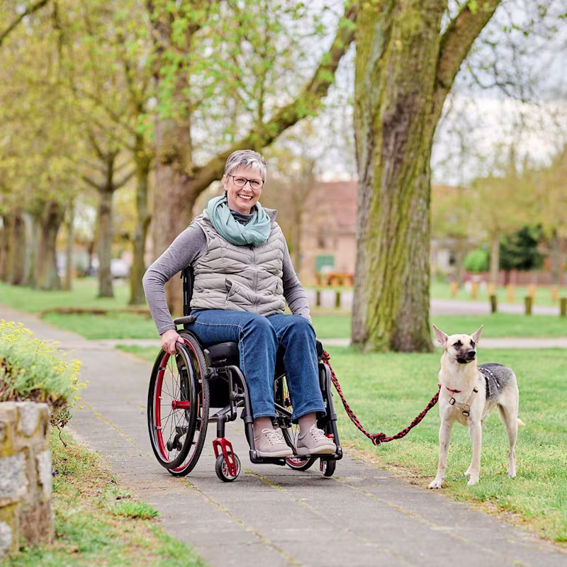Kırmızı Avantgarde manuel tekerlekli sandalyesinde oturan Wander, köpeğinin tasmasını tutuyor.