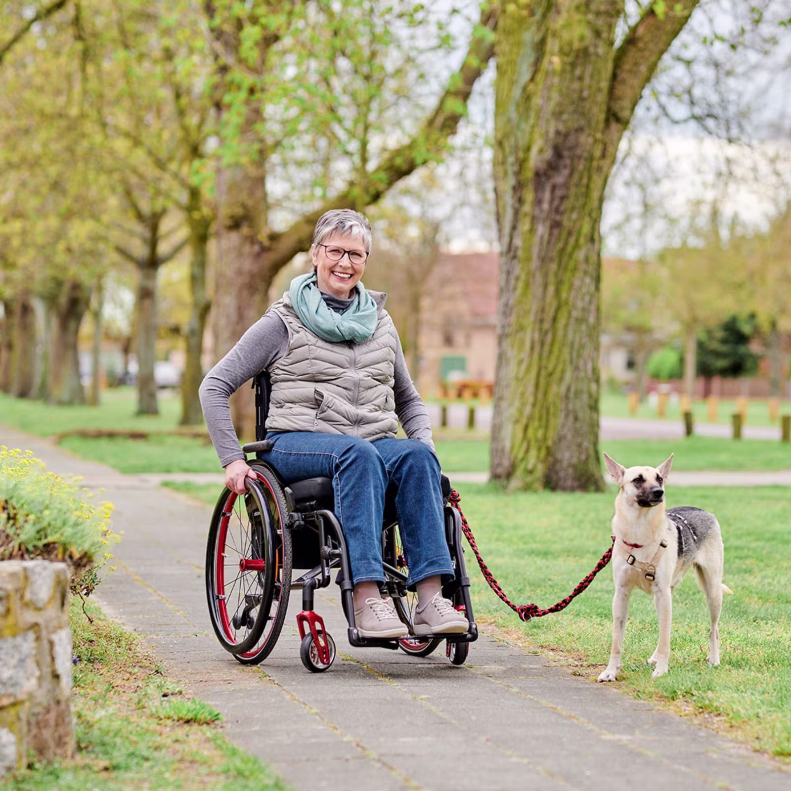 Wander sitting in her red Avantgarde 4 manual wheelchair holding the lead of her dog.