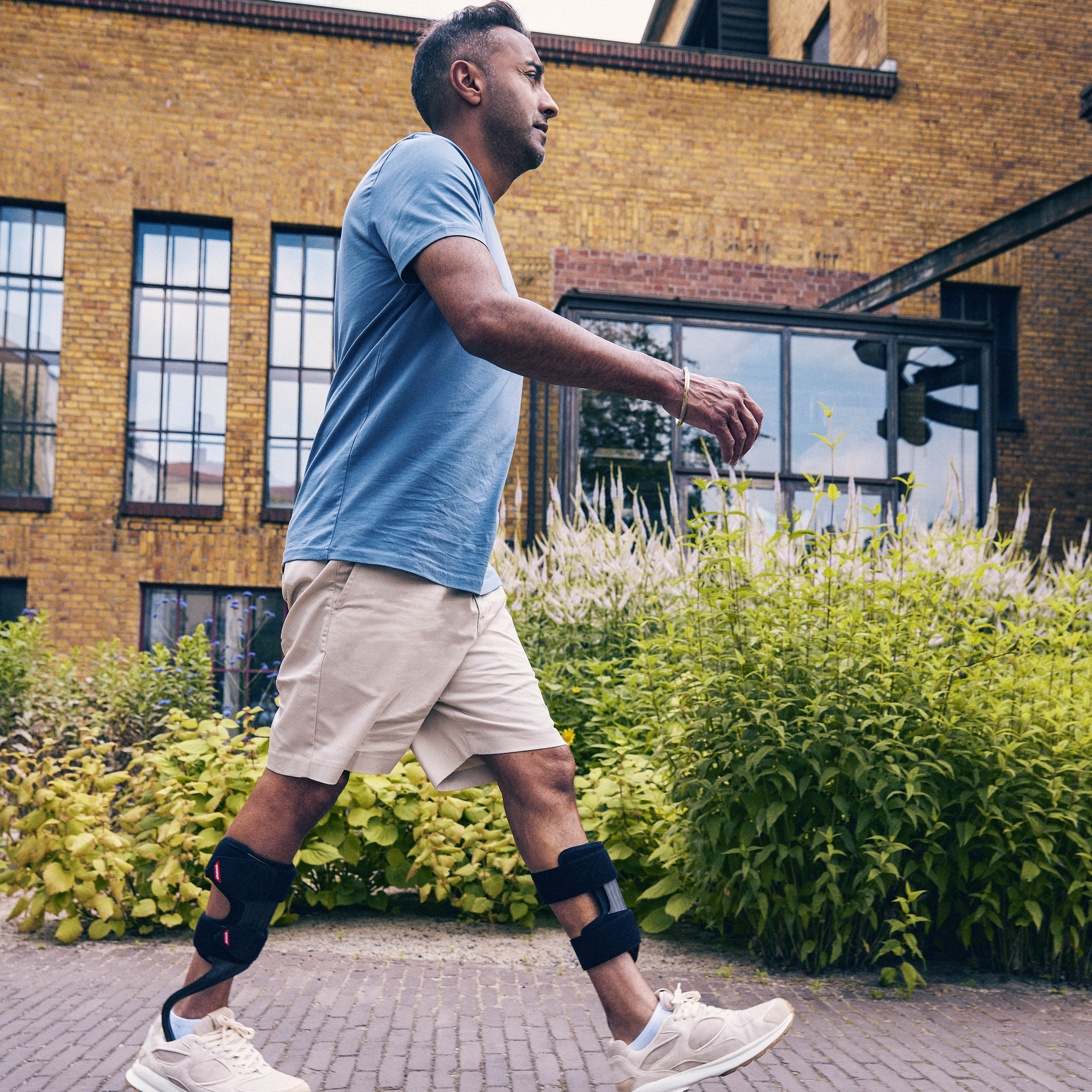 A man wearing two WalkOn ankle foot orthoses while walking on a street