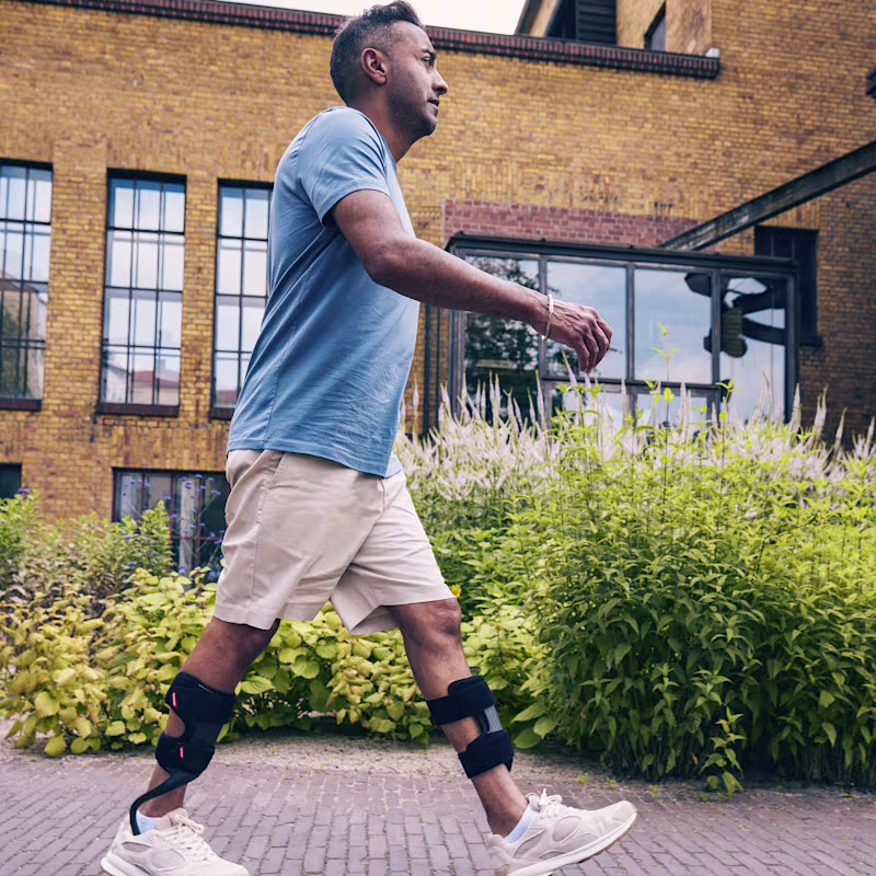A man wearing two WalkOn ankle foot orthoses while walking on a street