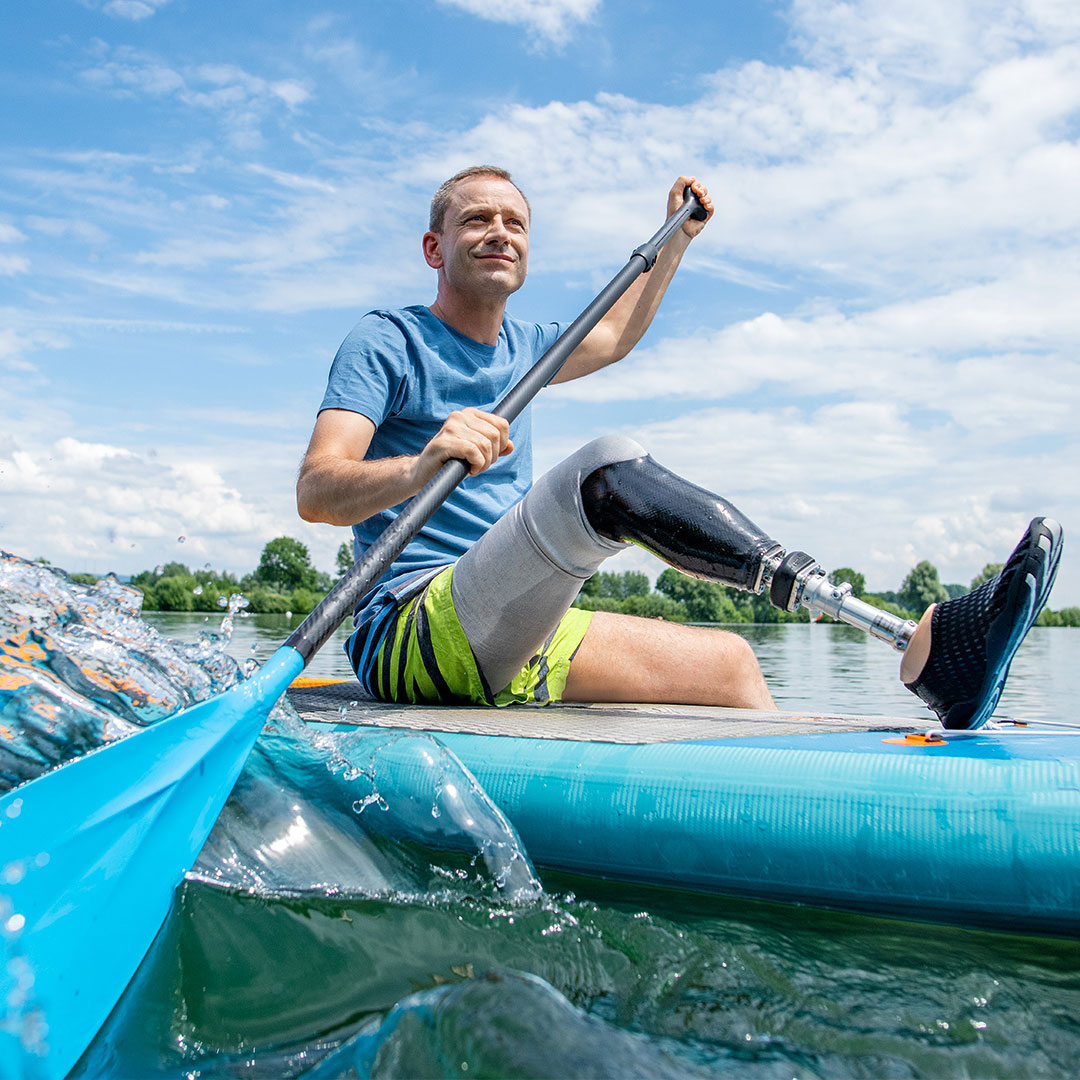 Un homme naviguant à travers un lac sur une planche de stand-up paddle tout en portant son pied prothétique résistant à l’eau, le Taleo d’Ottobock