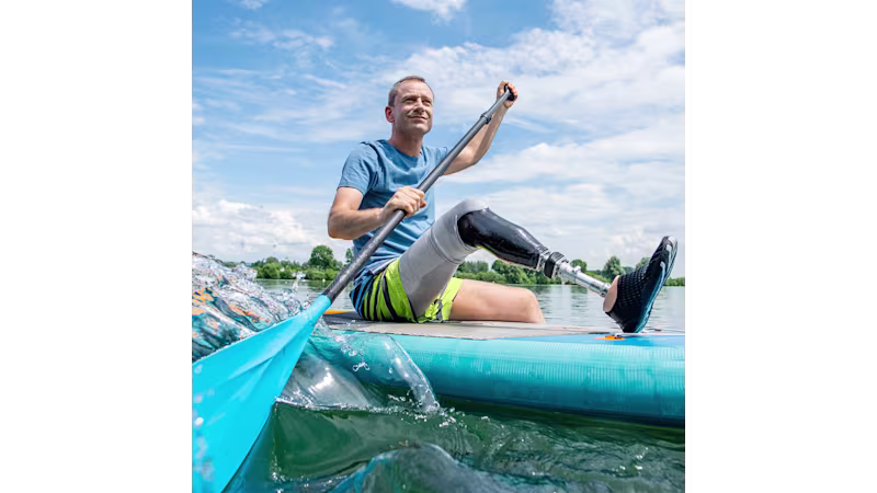 A man navigating through a lake on a stand-up paddle board while wearing his water-resistant prosthetic foot, the Taleo by Ottobock