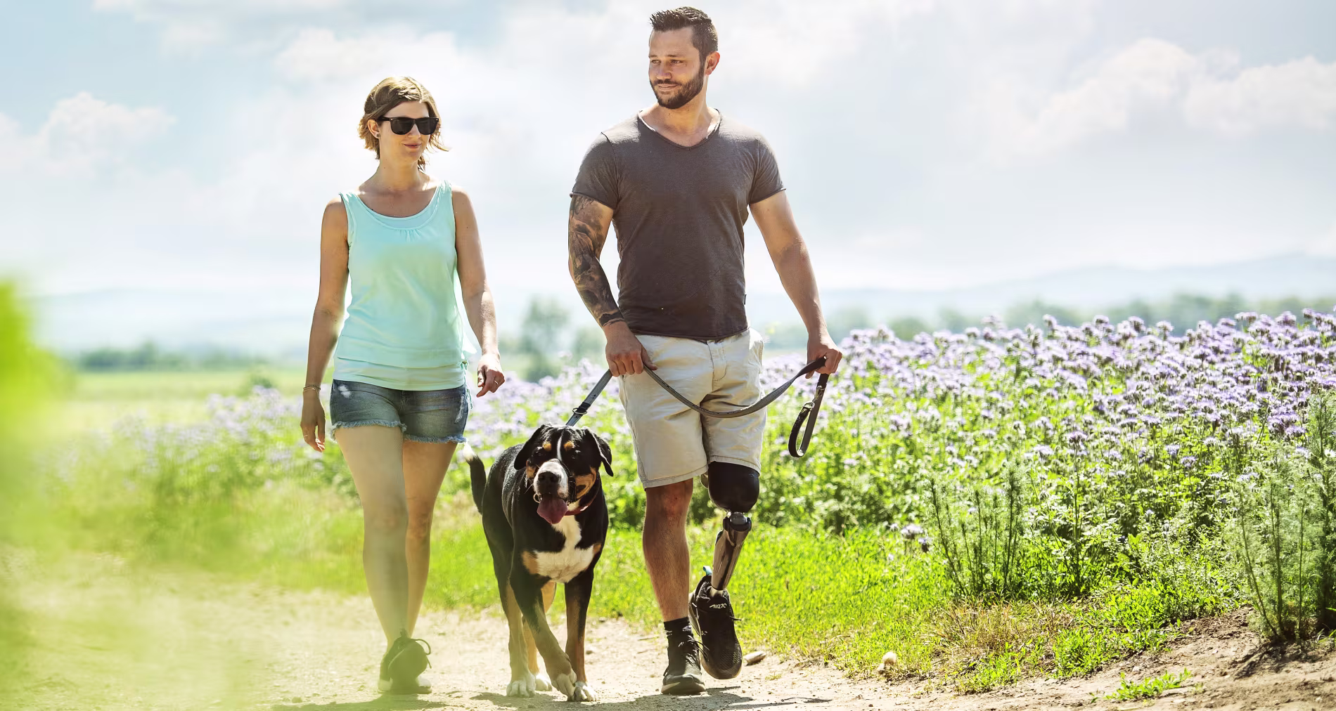 A couple walking their dog outside through a field of purple flowers using their custom Ottobock-manufactured C-Leg