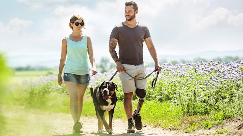 A couple walking their dog outside through a field of purple flowers using their custom Ottobock-manufactured C-Leg