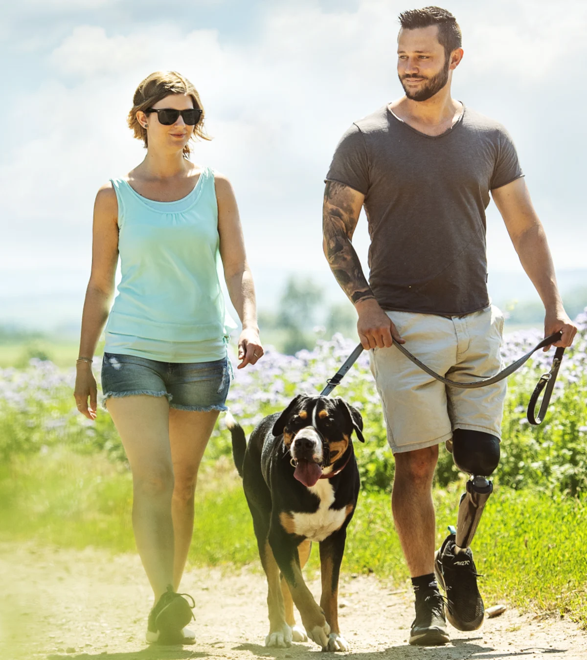 A couple walking their dog outside through a field of purple flowers using their custom Ottobock-manufactured C-Leg 
