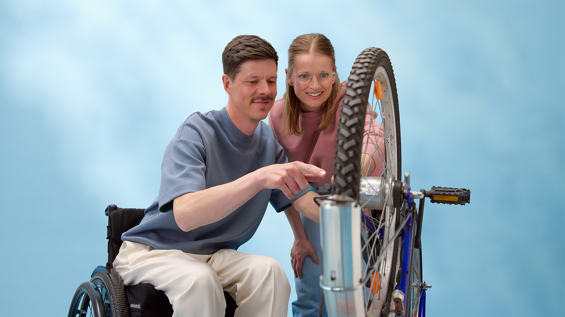 Person wearing an Ottobock exopulse suit smilingly playing Keyboard at a desk in front of a blue curtain