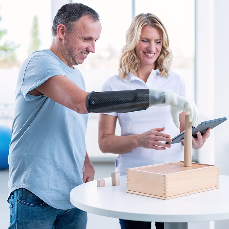 Eine Therapeutin trainiert mit einem amputierten Mann die Benutzung seiner michelangelo Prothesenhand von Ottobock.